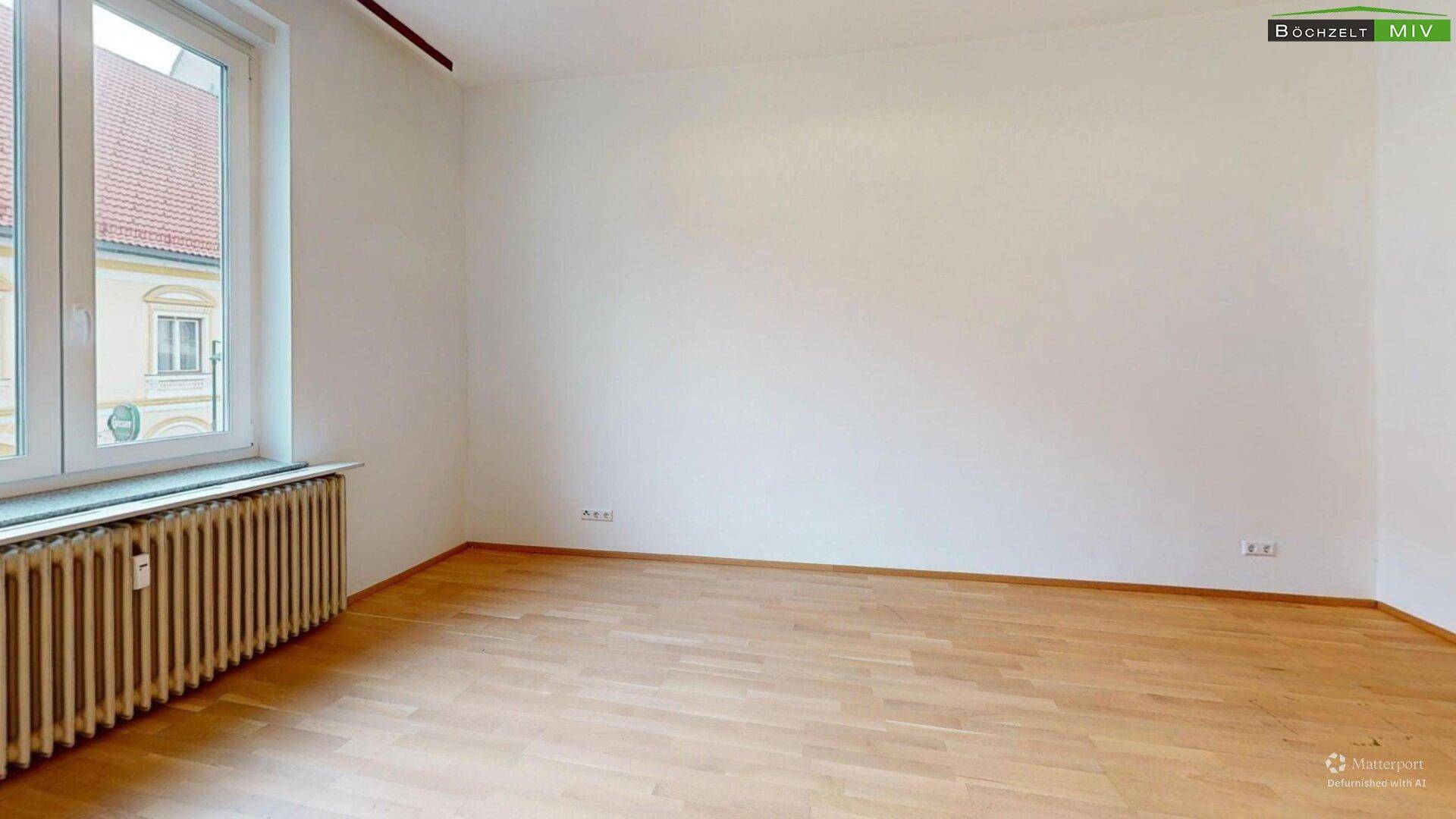 Helles Zimmer mit Parkettboden, großem Fenster und Blick nach draußen.