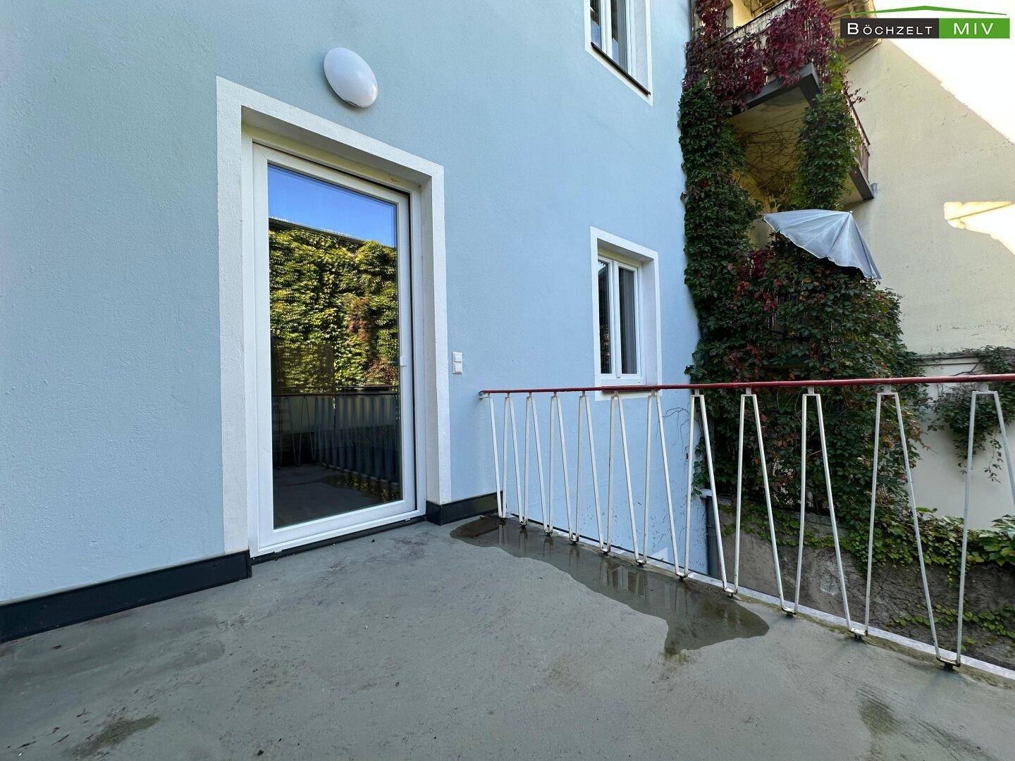 Kleiner Balkon mit weißem Geländer und Blick auf bewachsene Fassade.