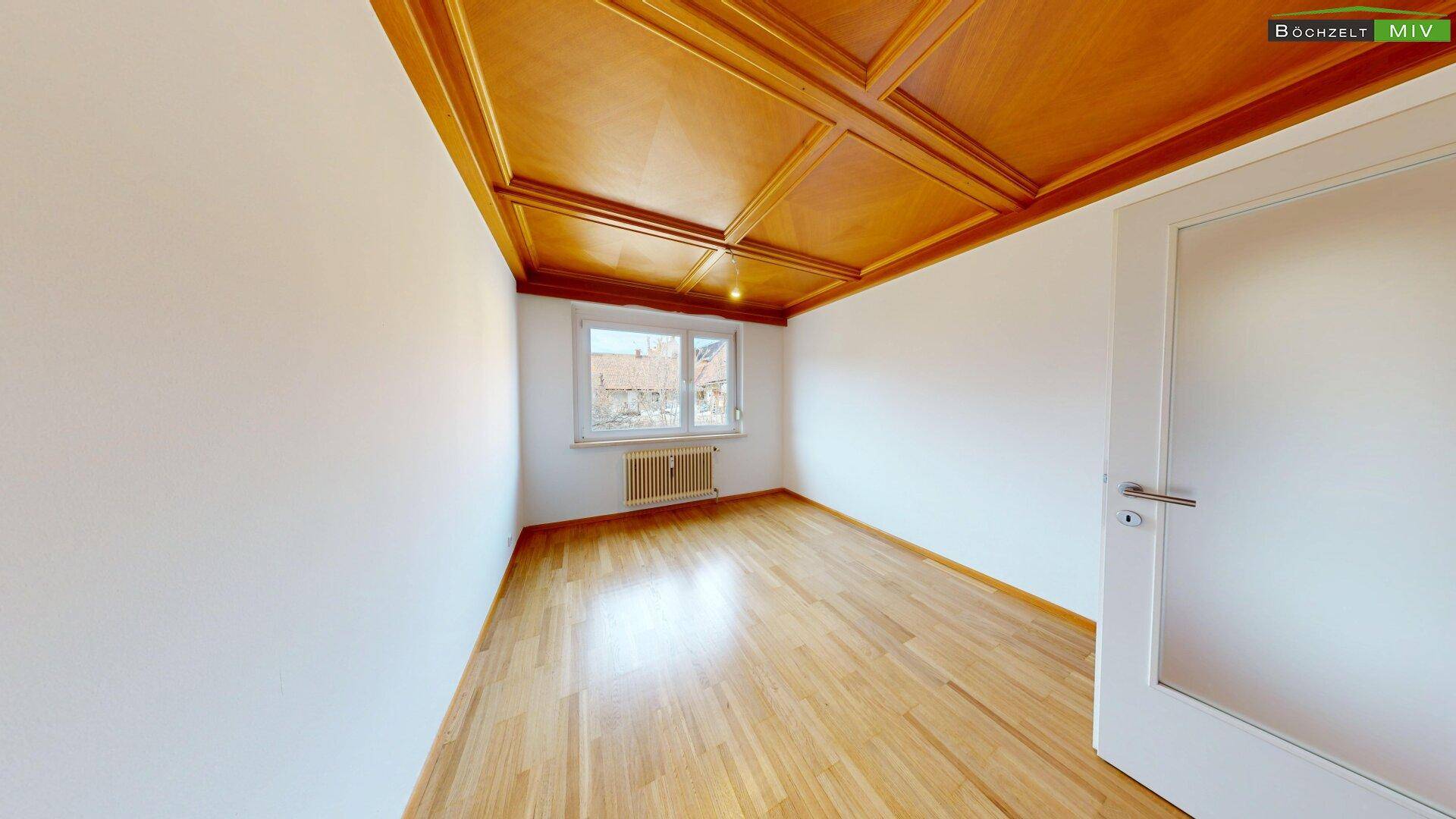 Geräumiges Zimmer mit klassischer Holzkassettendecke, Parkettboden und Fenster.