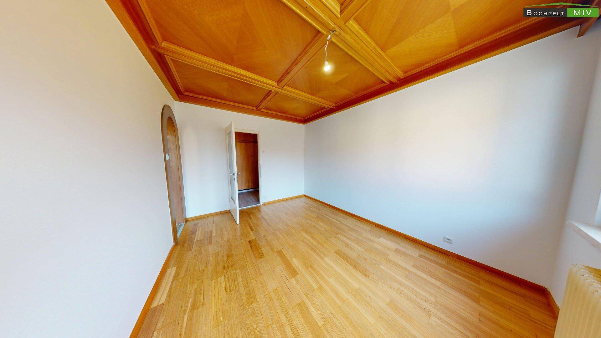 Zimmer mit traditioneller Holzkassettendecke, Parkettboden und Zugang zu einem weiteren Raum.