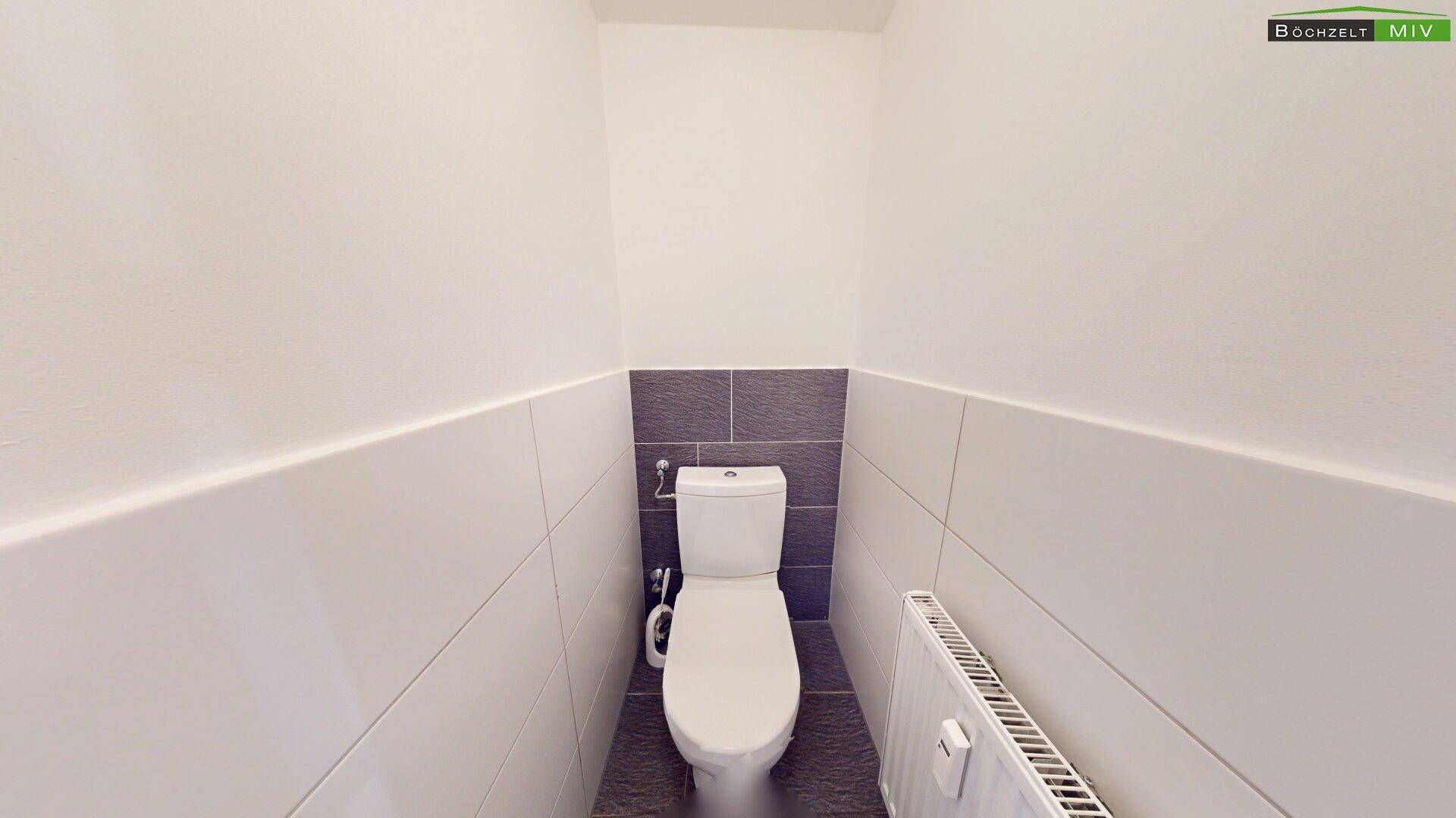 Separates WC mit Fliesenboden und Wandfliesen in Weiß und Grau.