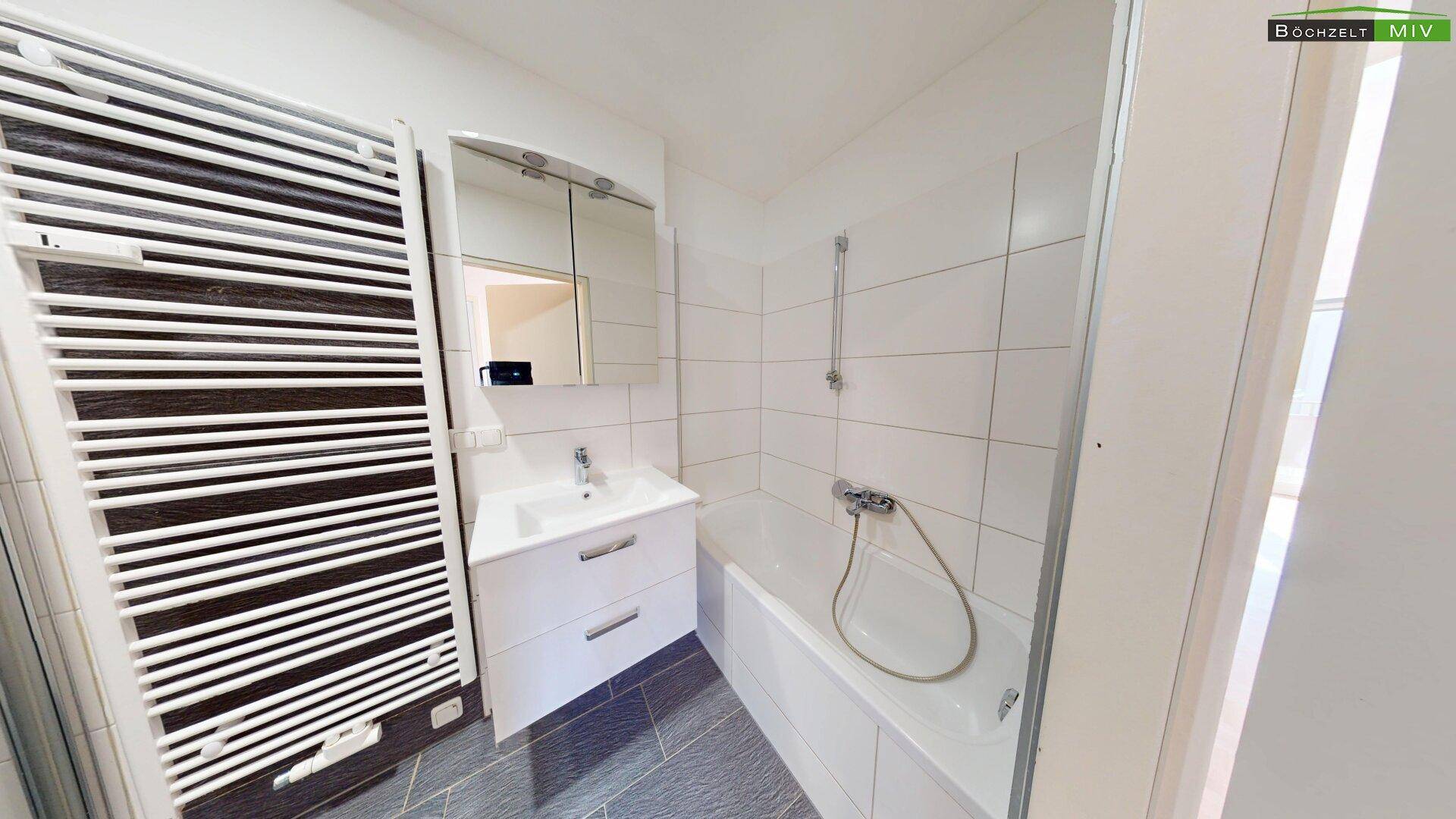 Badezimmer mit Badewanne, Waschbecken, Spiegelschrank und beheiztem Handtuchhalter.
