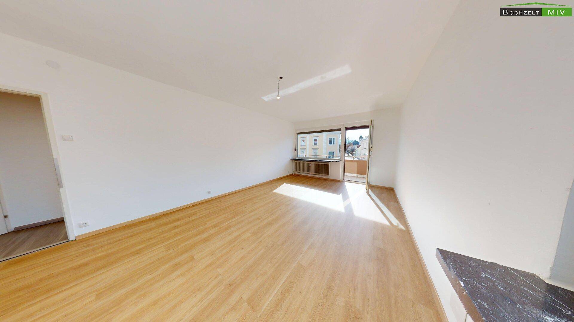 Helles Wohnzimmer mit Laminatboden, großen Fenstern und Zugang zum Balkon.