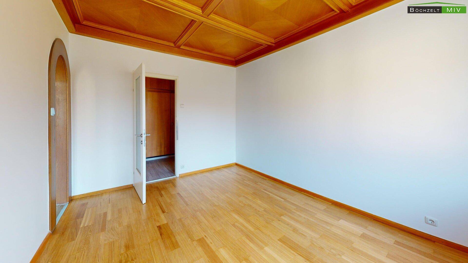 Zimmer mit charakteristischer Holzkassettendecke, Parkettboden und Türöffnung.