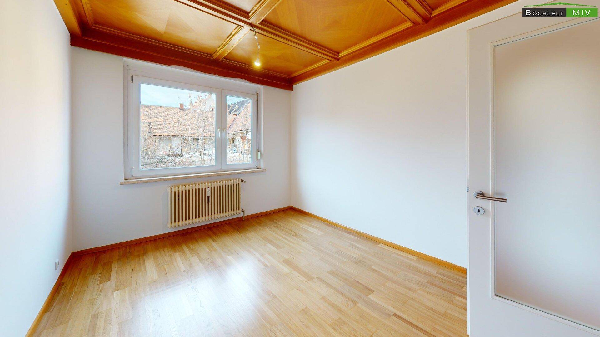 Geräumiges Zimmer mit Holzkassettendecke, Parkettboden und Blick nach draußen.