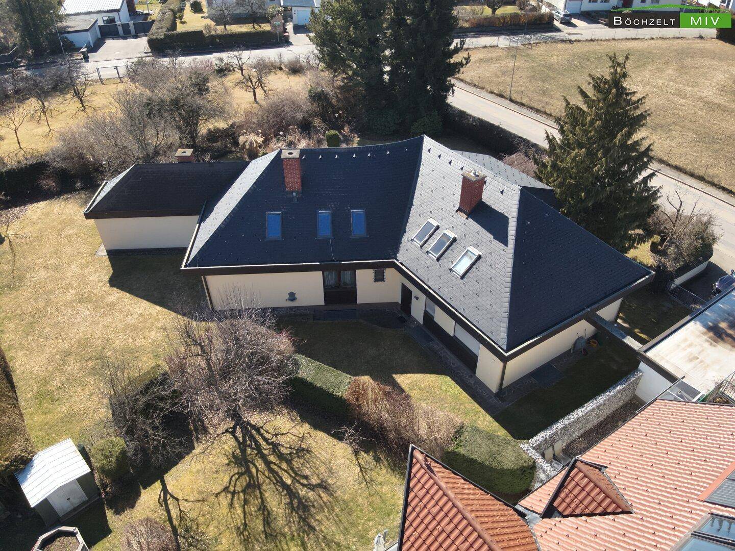 Vogelperspektive eines Einfamilienhauses mit dunklem Satteldach, Dachfenstern und gepflegtem Gartenbereich.