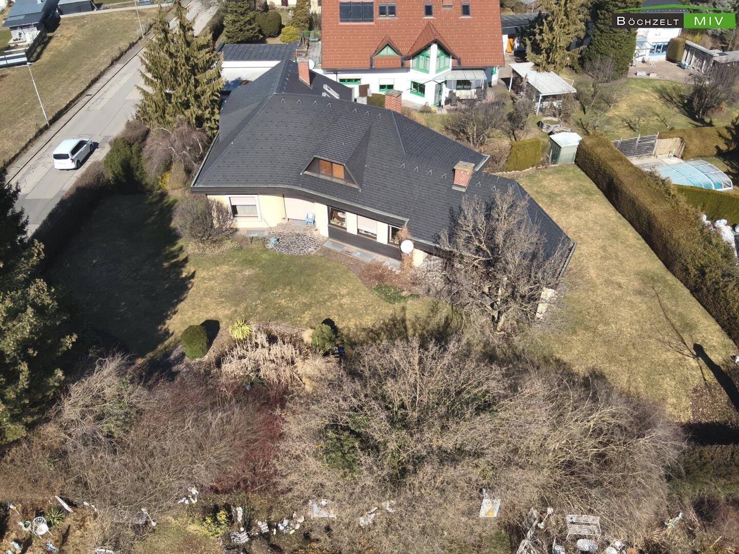 Luftaufnahme eines Einfamilienhauses mit großem Garten und umliegender Wohnbebauung in sonniger Lage.