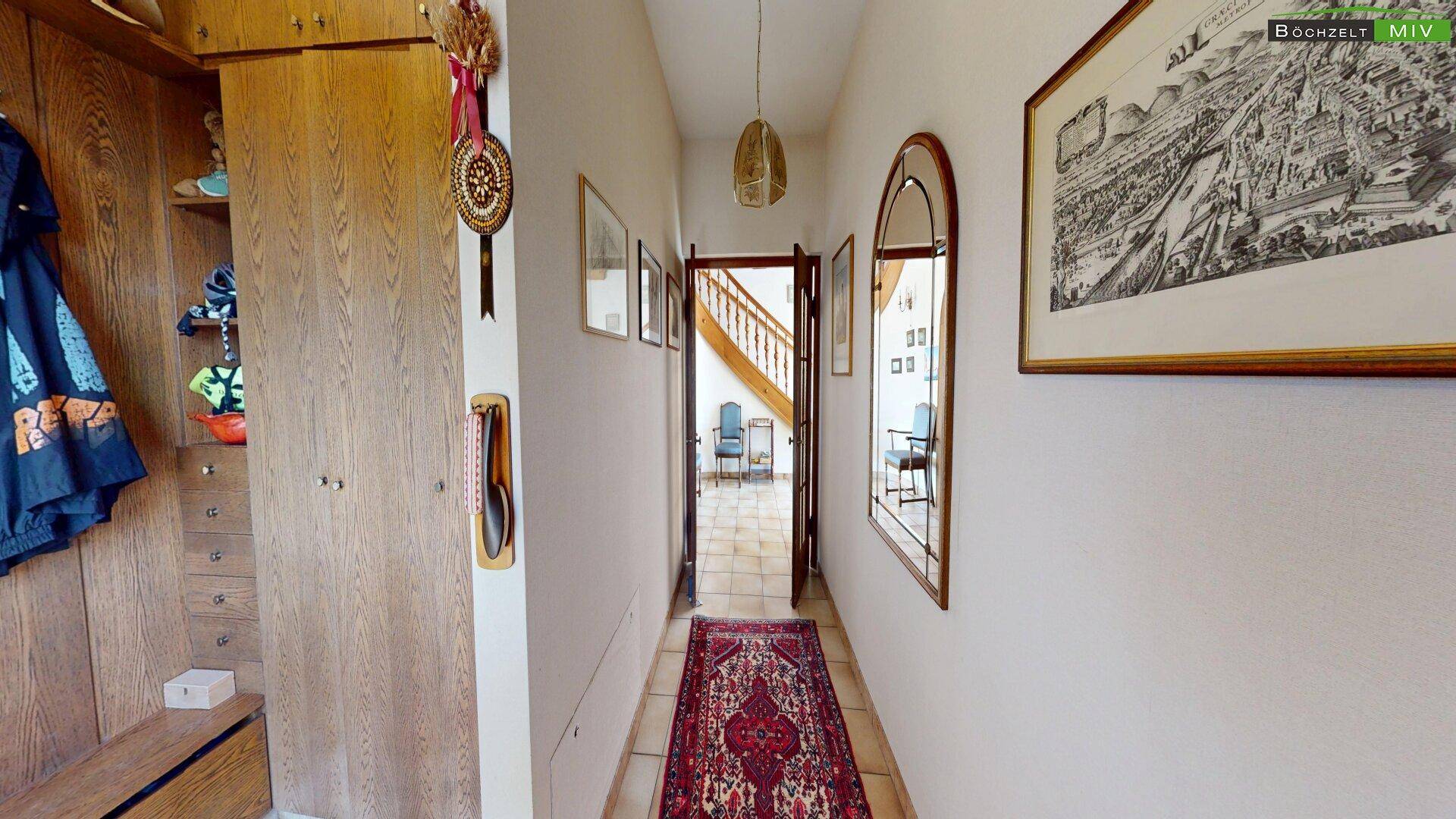 Heller Flur mit Terrakotta-Fliesen, Garderobe und einem Spiegel, der den Blick auf die Treppe freigibt.
