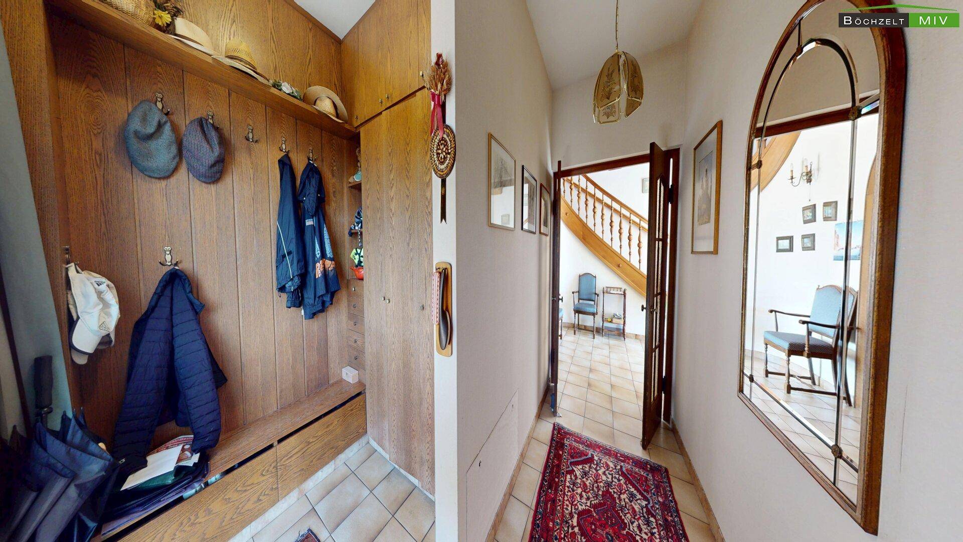 Eingangsbereich mit Holzvertäfelung, Garderobe und einem Teppich auf den Terrakotta-Fliesen.