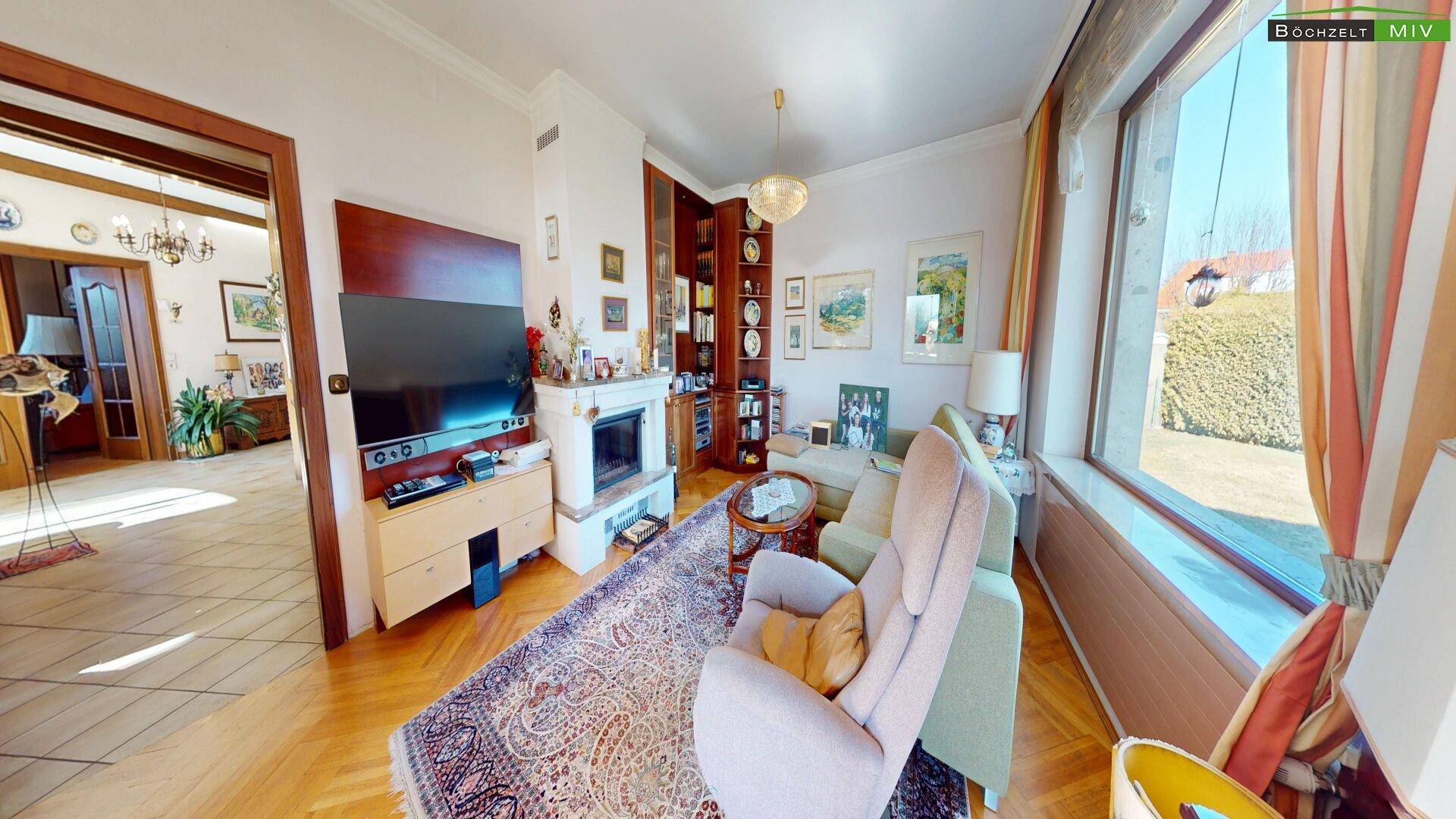 Wohnzimmer mit Parkettboden, Kamin und großen Fenstern, die viel Tageslicht hereinlassen.