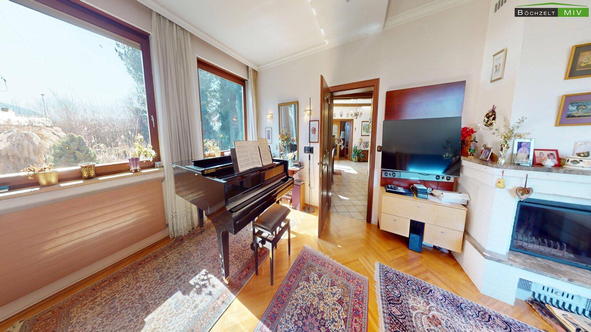 Helles Wohnzimmer mit Parkettboden, Flügel und großen Fenstern mit Blick in den Garten.