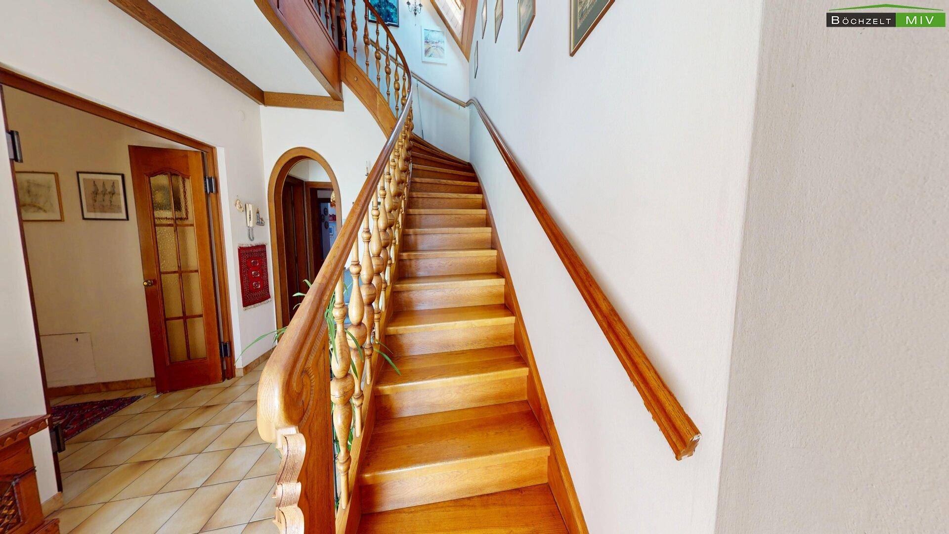 Elegantes Treppenhaus mit Holzgeländer und gefliestem Boden, das in die obere Etage führt.