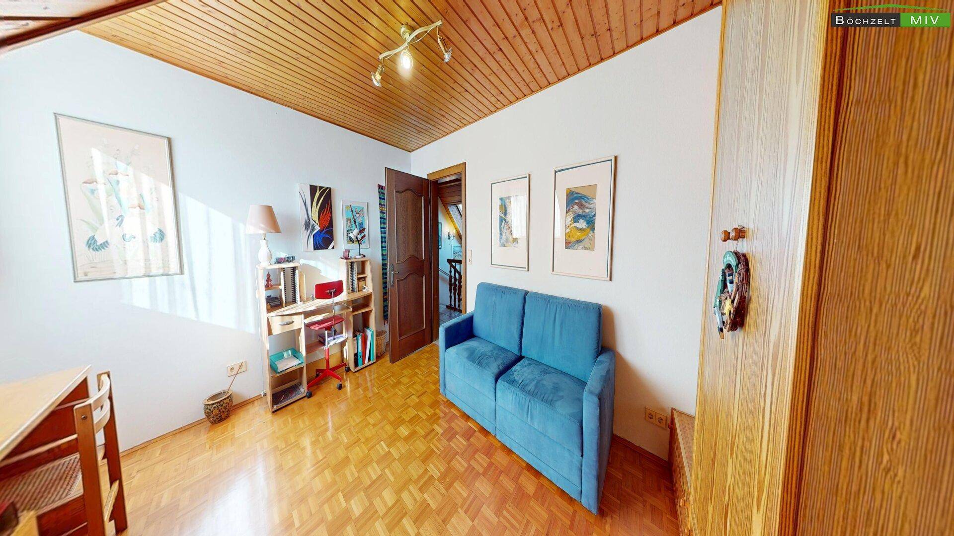 Helles Arbeitszimmer mit Holzdecke, Parkettboden und blauem Sofa.