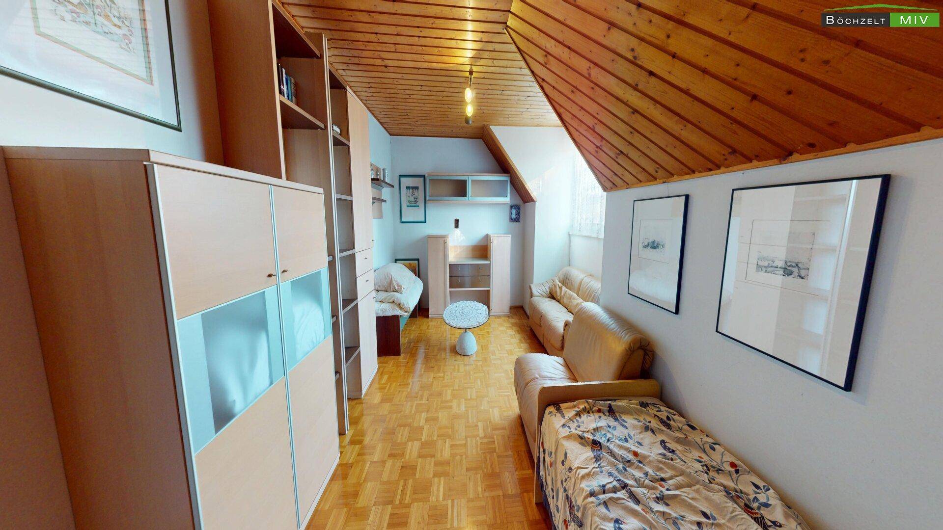 Gemütliches Wohnzimmer im Dachgeschoss mit Holzdecke, Parkettboden und Sofa.