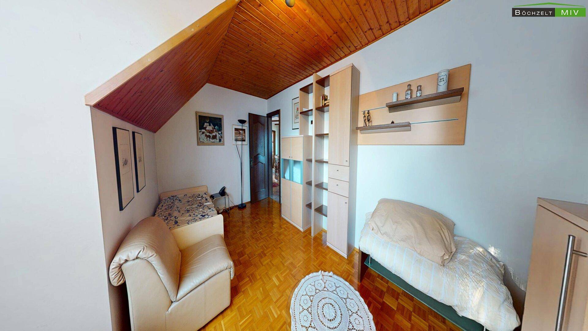 Helles Wohnzimmer im Dachgeschoss mit Holzdecke, Parkettboden und Sitzgelegenheiten.