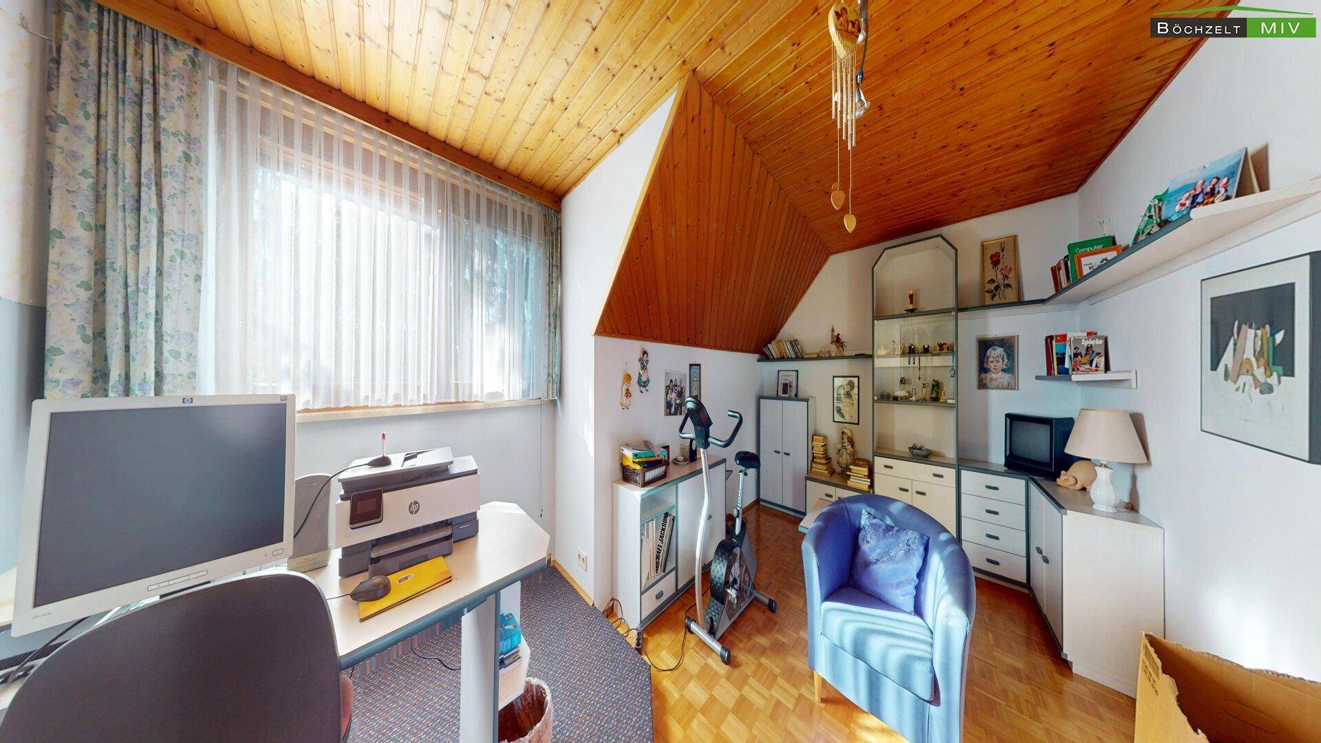 Helles Arbeitszimmer im Dachgeschoss mit Schreibtisch, Sportgerät und Holzdecke.