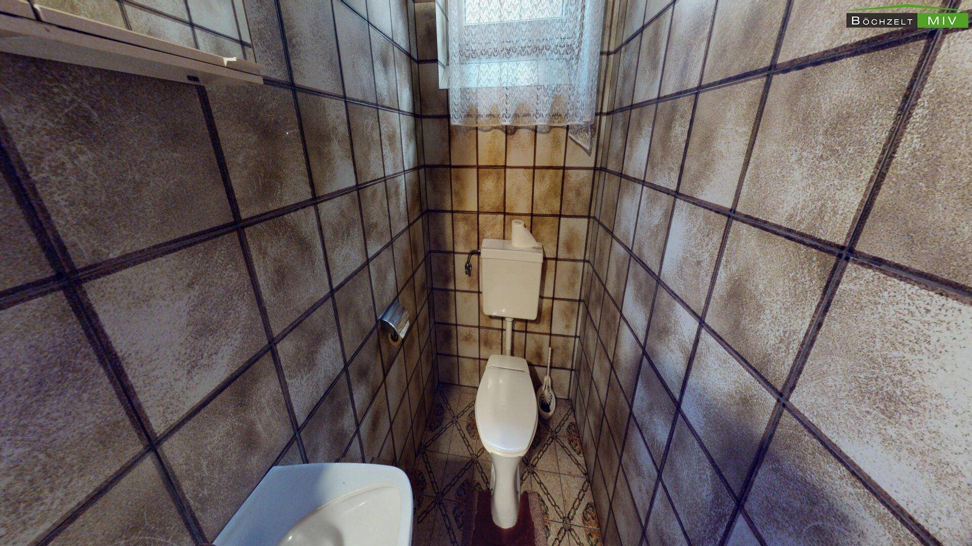 Kleines WC mit gefliesten Wänden und einem Fenster, das für Belüftung sorgt.