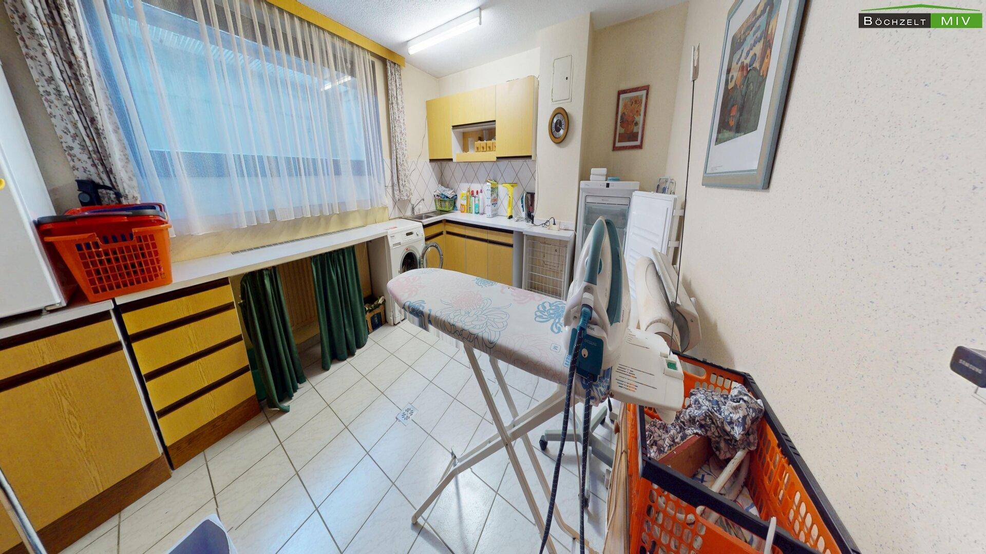 Praktischer Hauswirtschaftsraum mit Waschmaschine, Bügelbrett und gelben Küchenschränken.