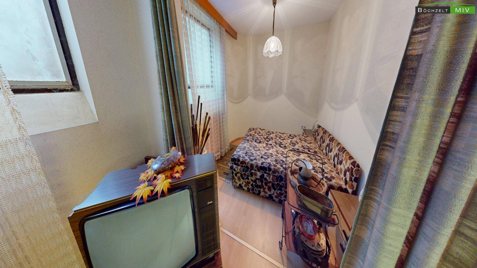 Schlafzimmer mit einem gemusterten Schlafsofa, einem Vintage-Fernseher und Holzboden.