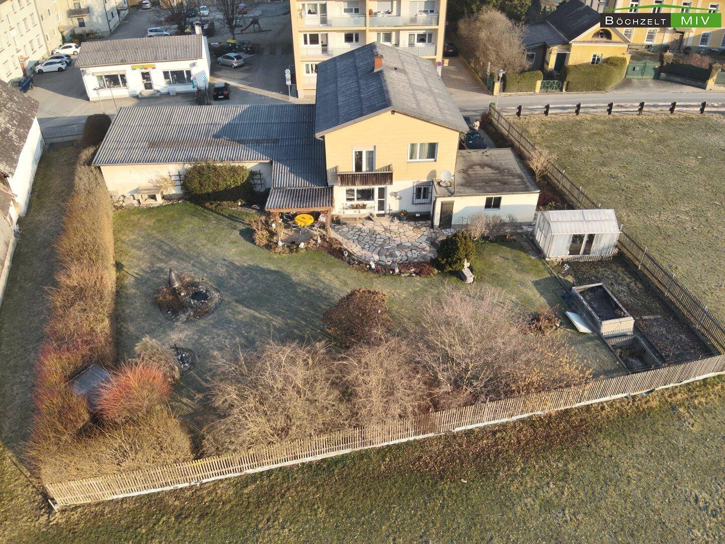 Weitläufiger Gartenbereich mit Rasenfläche, Sträuchern und einem kleinen Gewächshaus hinter dem Haus.