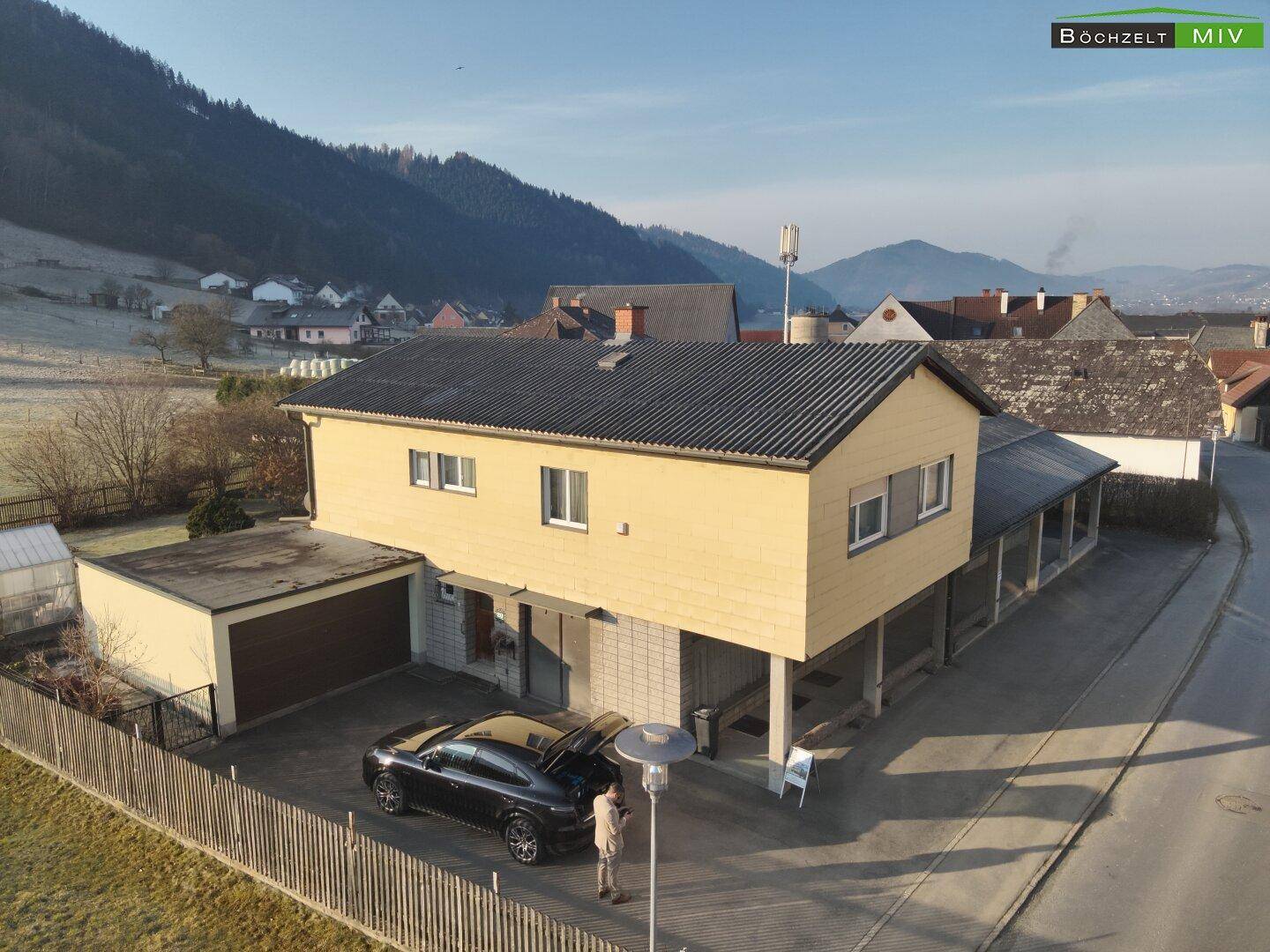 Luftaufnahme des Einfamilienhauses mit Garage und einem Auto auf dem Vorplatz vor Bergkulisse.