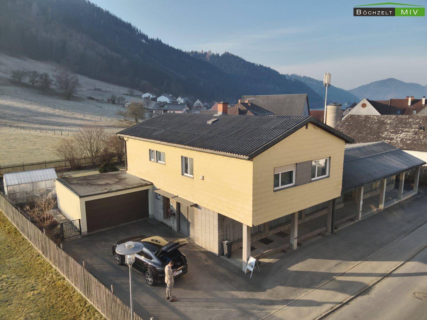 Übersicht des Wohnhauses mit Garage und gepflasterter Einfahrt, eingebettet in eine ländliche Landschaft.
