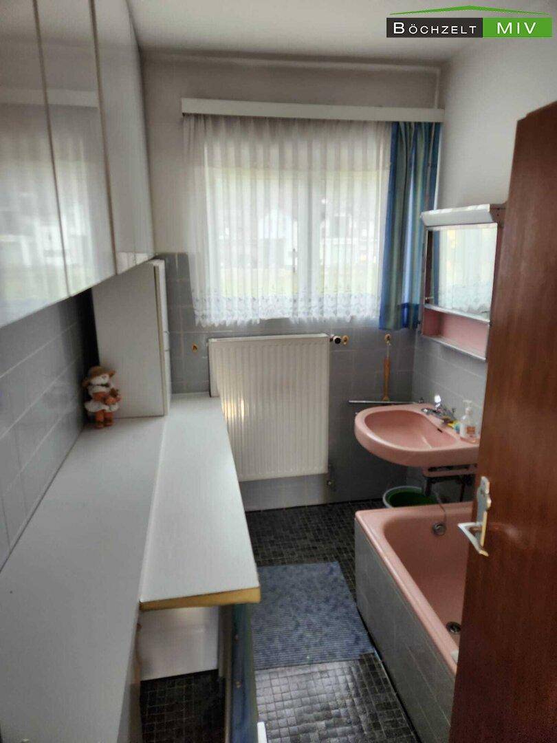 Badezimmer im Stil der 80er Jahre mit rosa Sanitärobjekten, grauen Fliesen und einem Fenster.