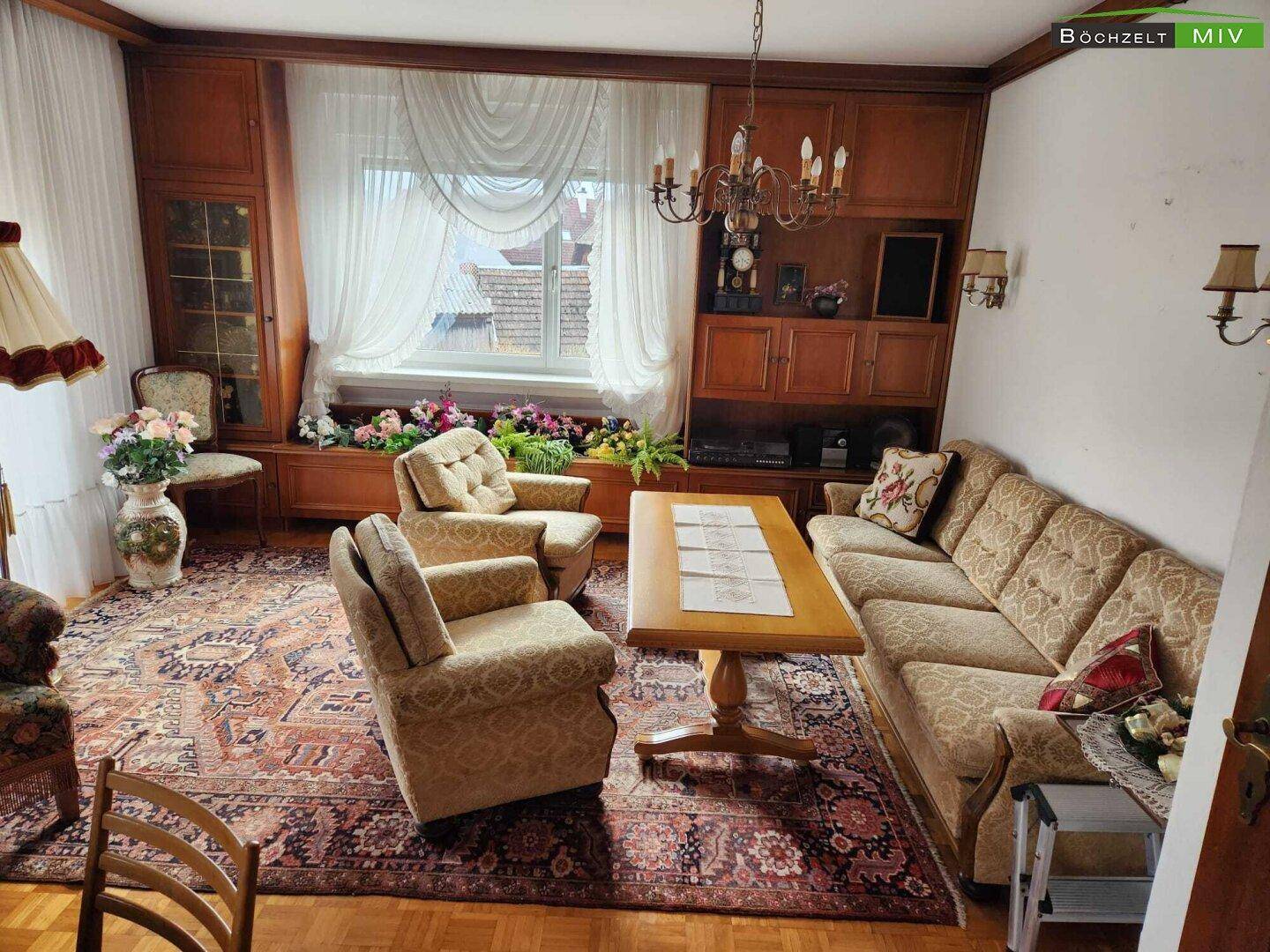 Klassisches Wohnzimmer mit bequemen Polstermöbeln, Holzeinbauten und einem großen Fenster.
