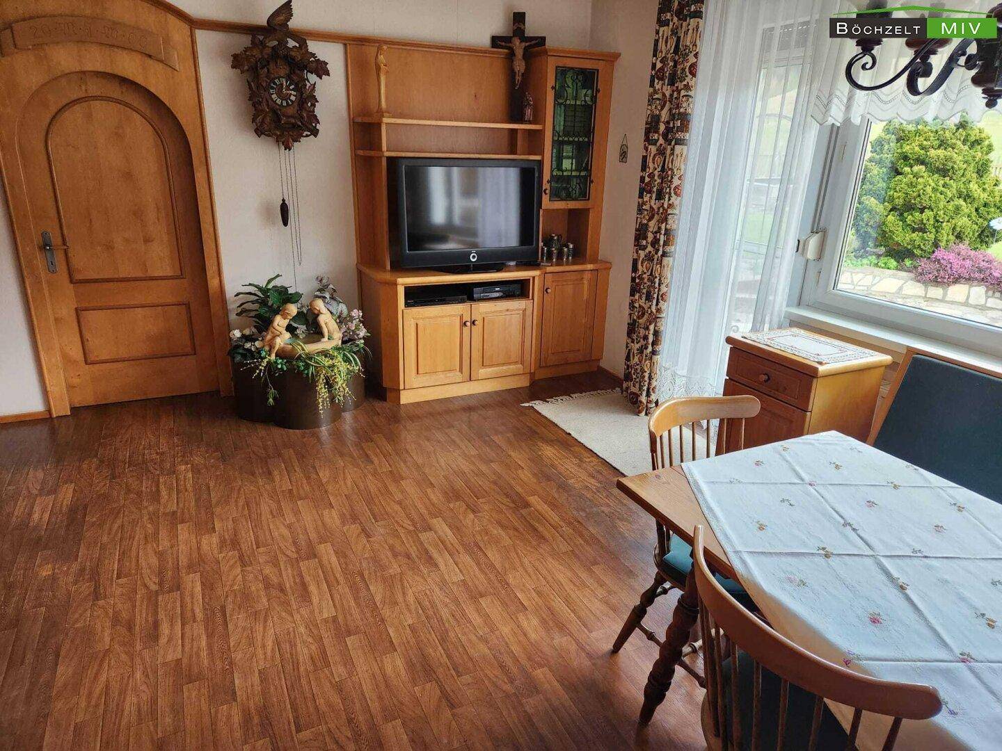 Gemütlicher Essbereich mit Holztisch, Stühlen und einem Fernseher, mit Blick ins Grüne.
