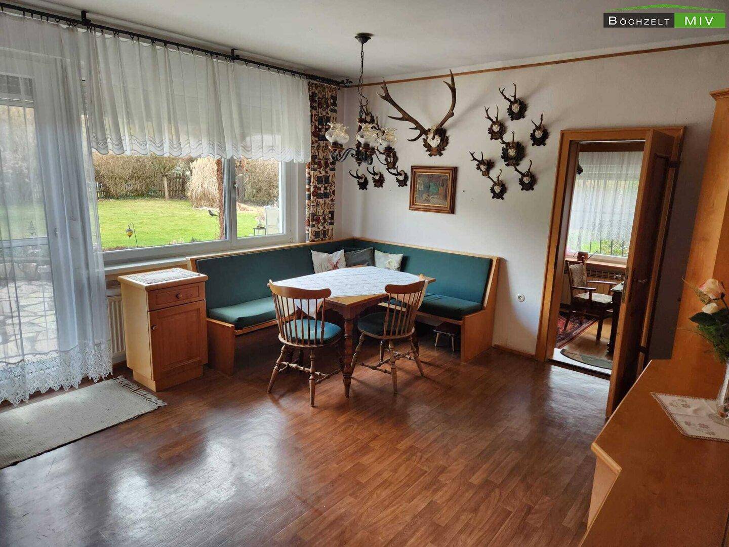 Essbereich mit Eckbank, Holztisch und traditioneller Dekoration, mit Blick in den Garten.