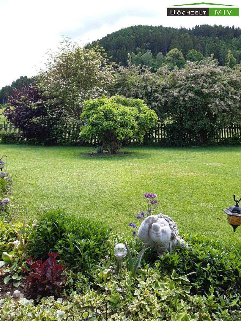 Großer, gepflegter Rasenbereich mit Blumenbeeten und einer Hecke, umgeben von grünen Hügeln.
