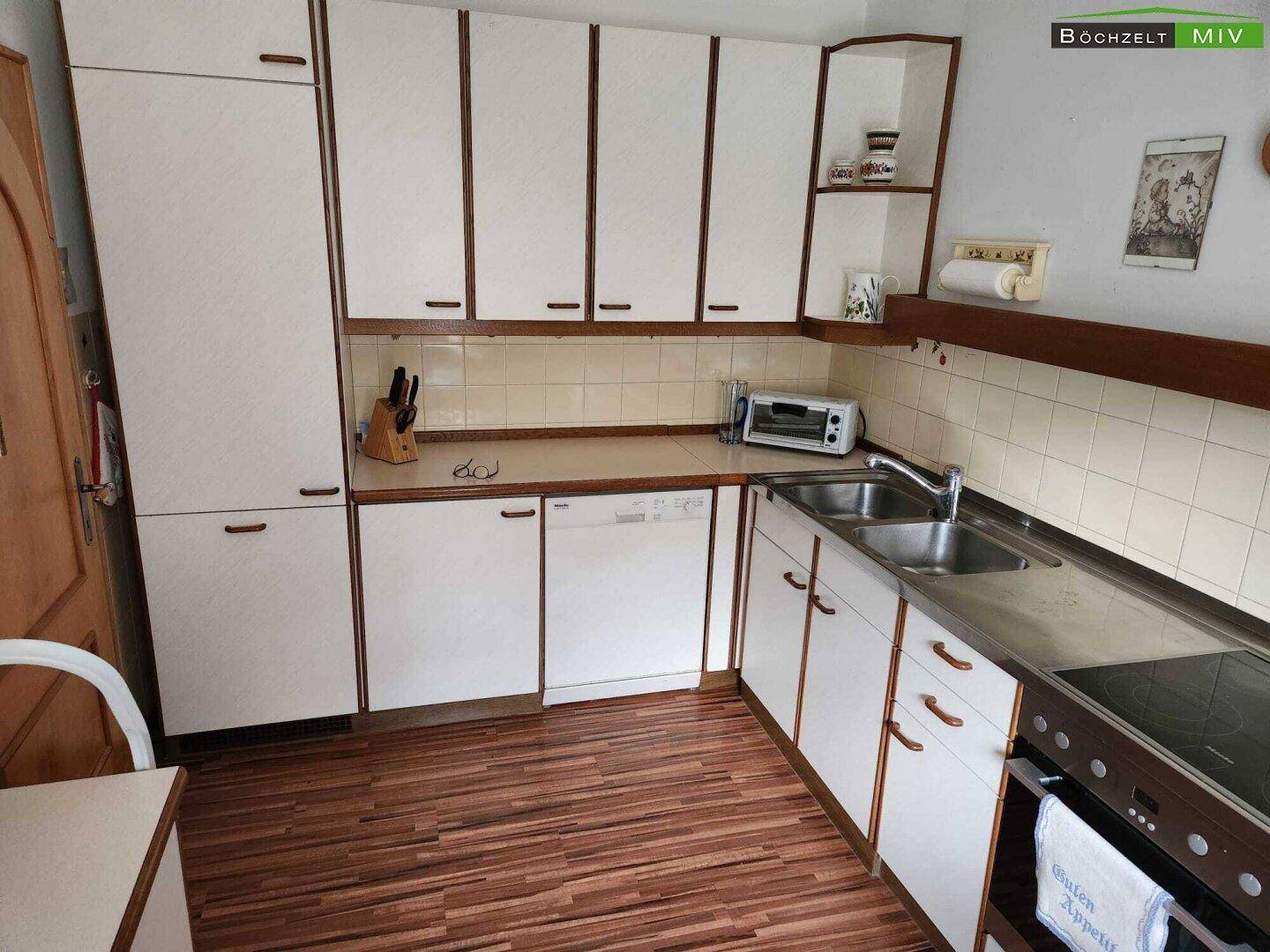 Funktionale Küche mit weißen Schränken, Holzdetails und integrierten Geräten.