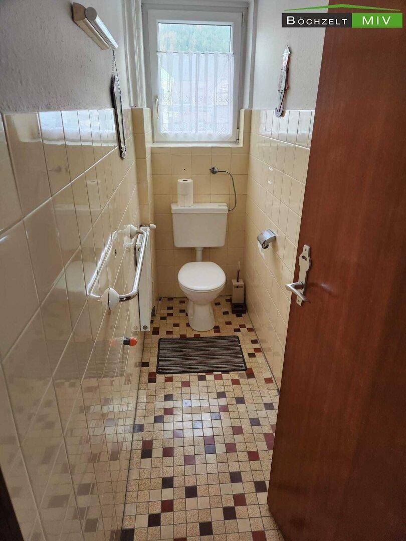 Kleines WC mit beigen Fliesen, Toilette und einem Fenster für natürliche Belüftung.
