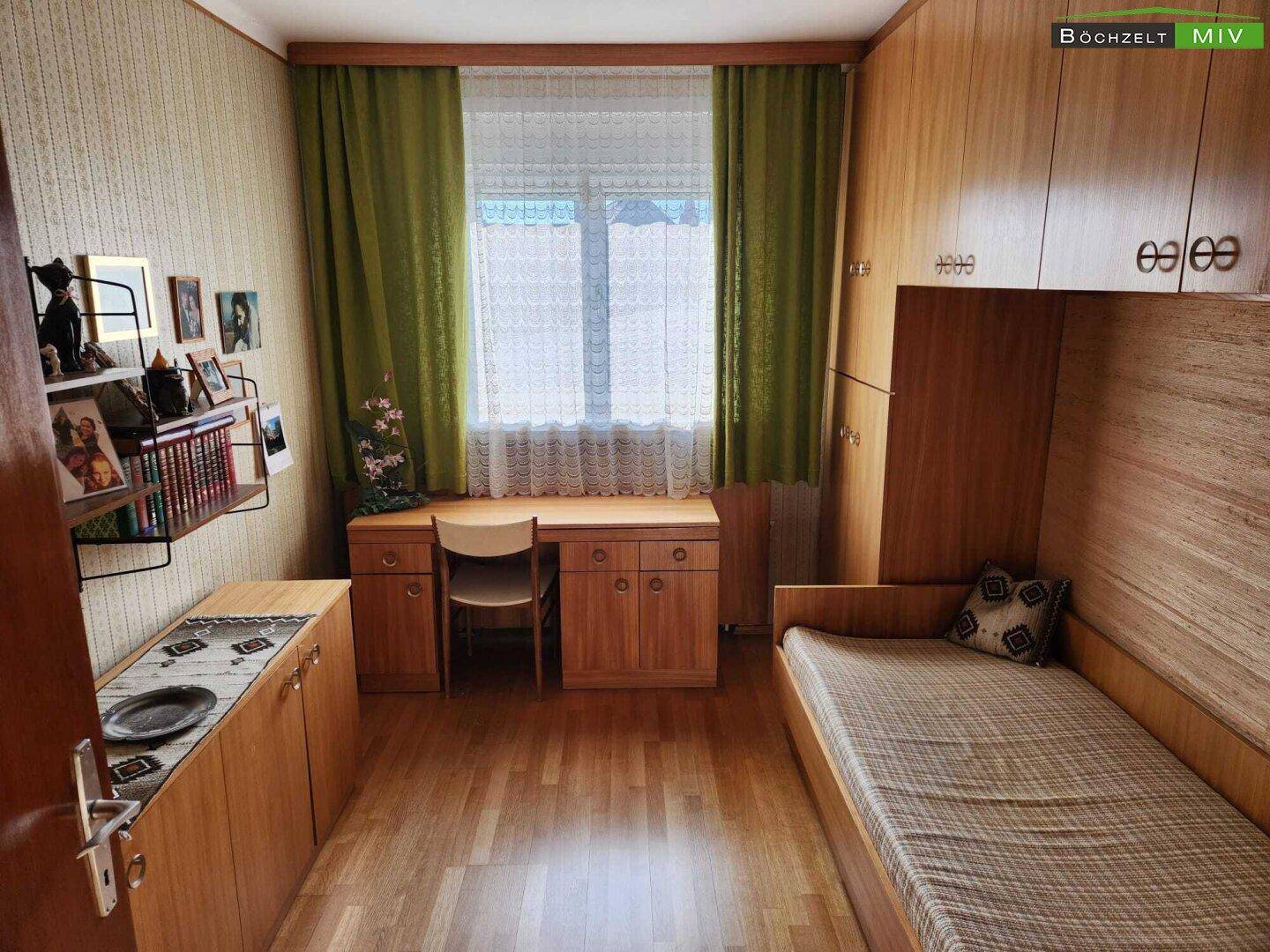 Helles Zimmer mit Einzelbett, Schreibtisch und Holzschränken, ideal als Kinder- oder Arbeitszimmer.