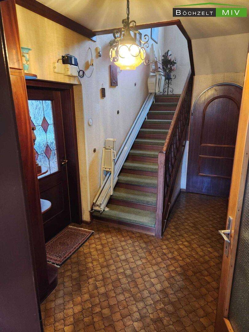 Geräumiger Flur mit Treppe, Holzgeländer und einem Treppenlift für Barrierefreiheit.