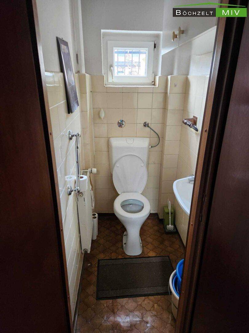 Kleines WC mit beigen Fliesen, Toilette und einem kleinen Waschbecken.