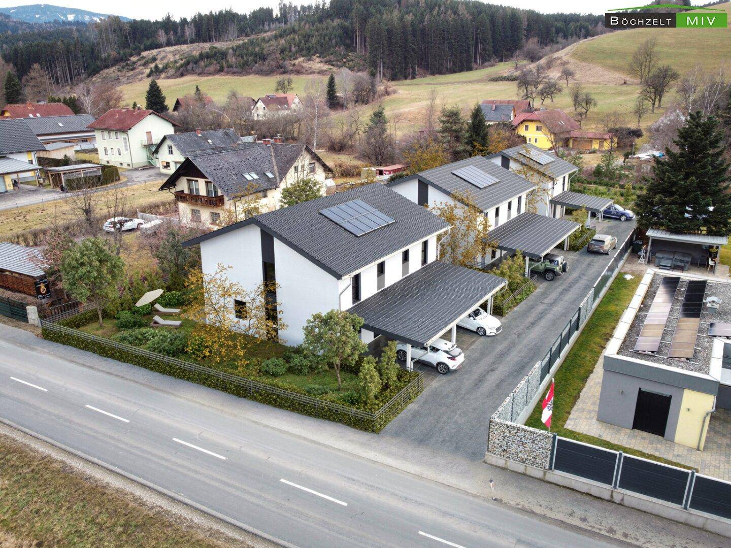 Luftaufnahme einer modernen Wohnsiedlung mit Doppelhäusern, Carports und Photovoltaikanlagen.