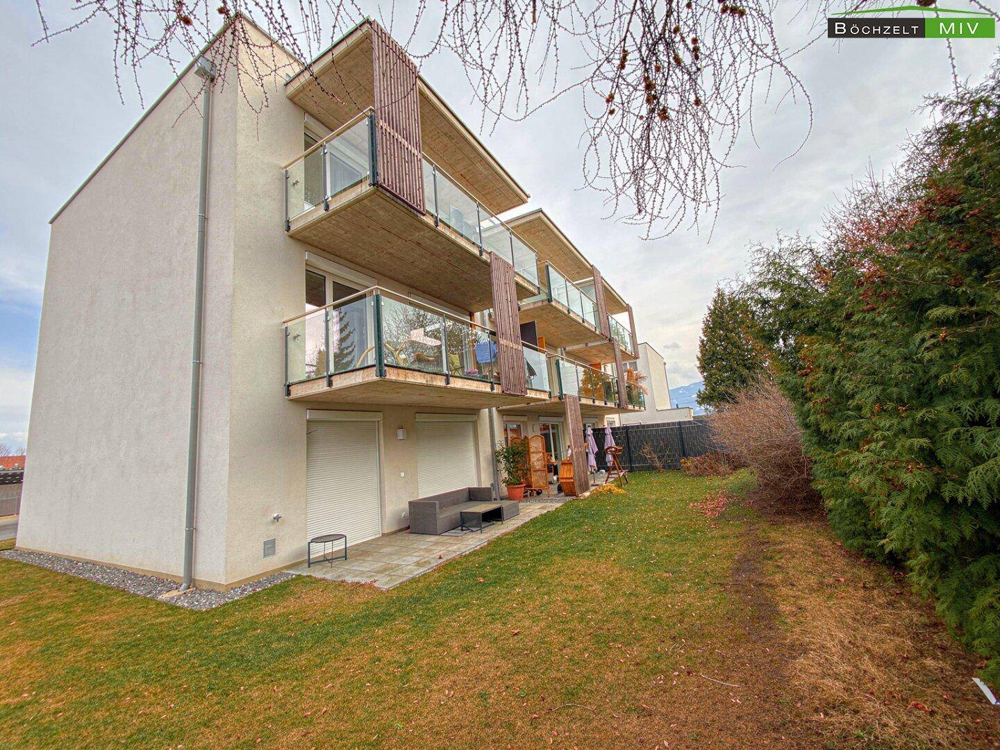 Seitenansicht eines modernen Wohngebäudes mit Balkonen und angrenzender Rasenfläche.