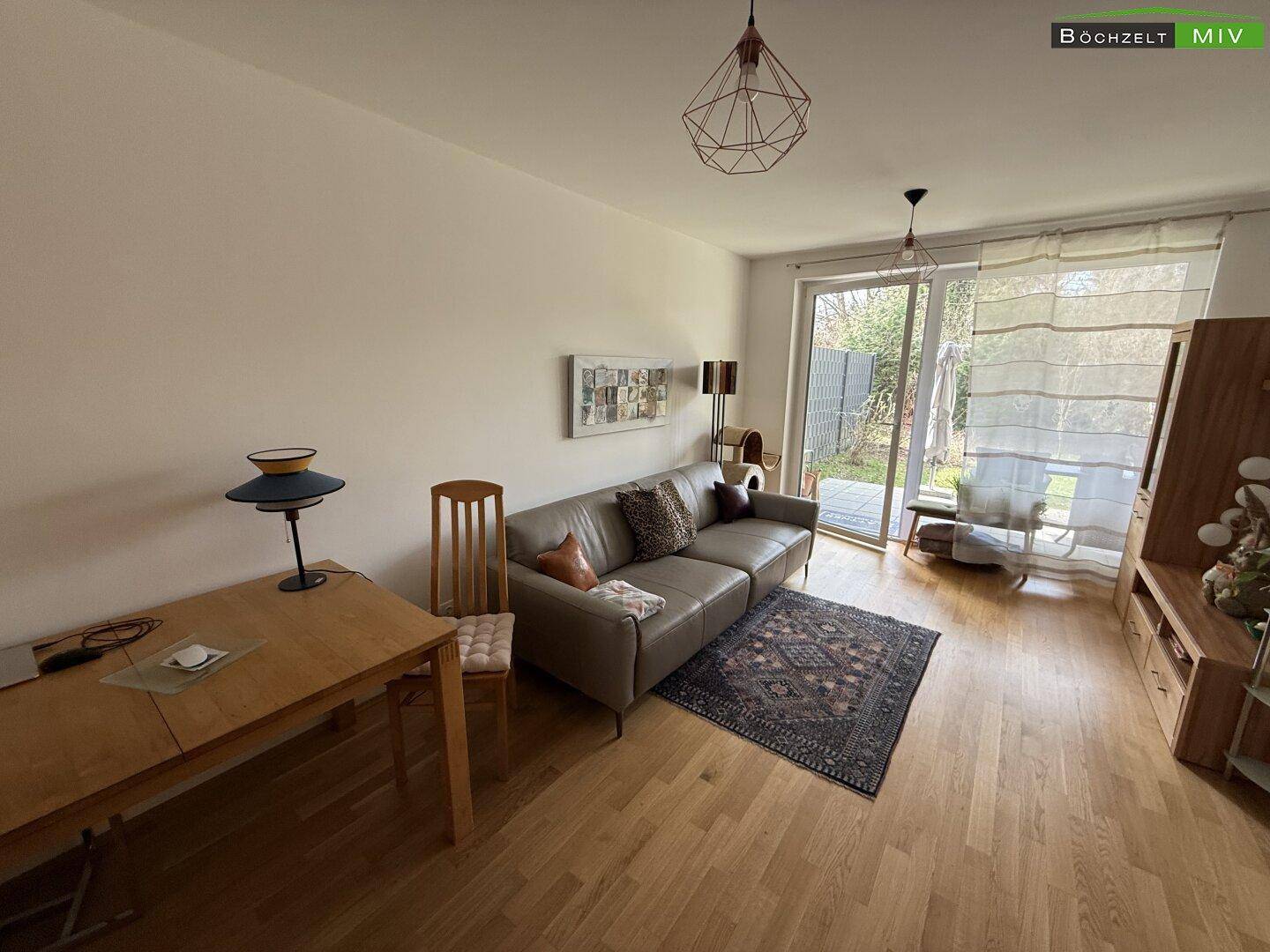 Helles Wohnzimmer mit Holzfußboden, bequemer Couch und Zugang zum Garten.