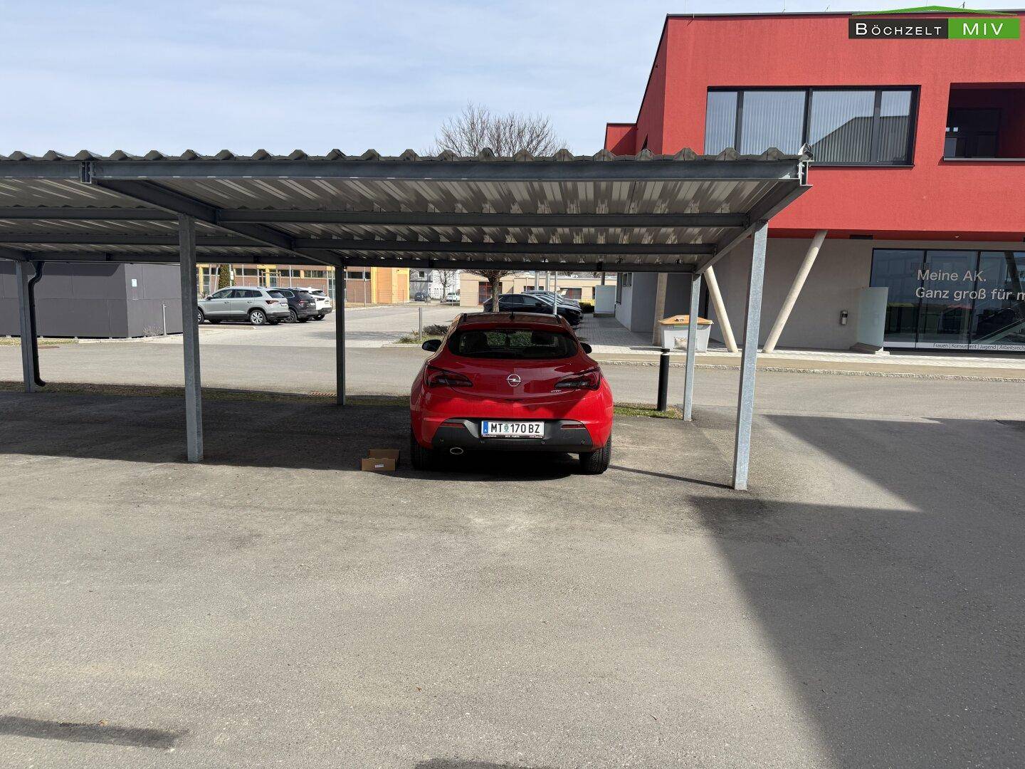 Überdachter Carport-Stellplatz mit einem geparkten roten Auto.