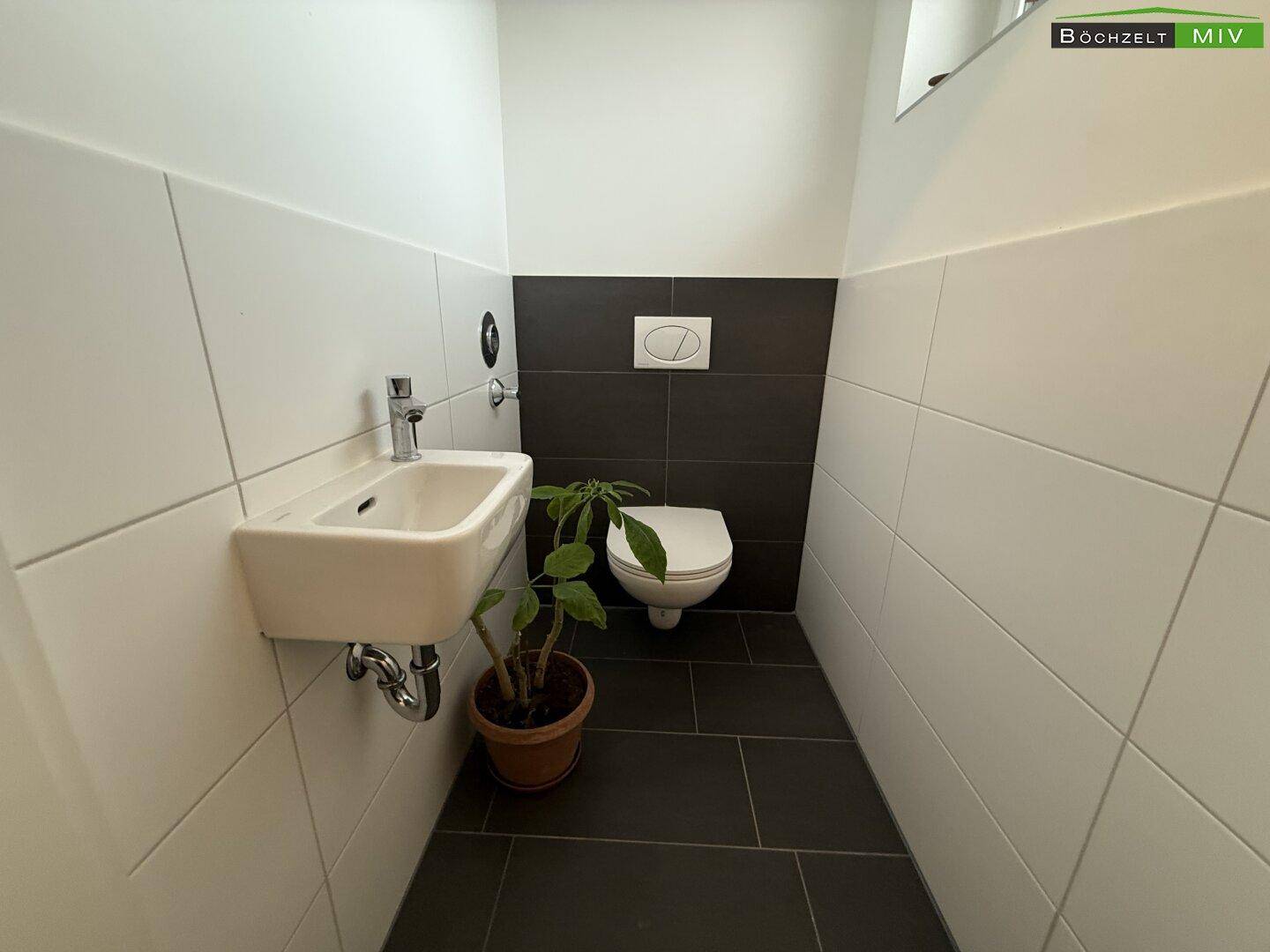 Modernes Gäste-WC mit dunklen Bodenfliesen und weiß-grauen Wandfliesen.