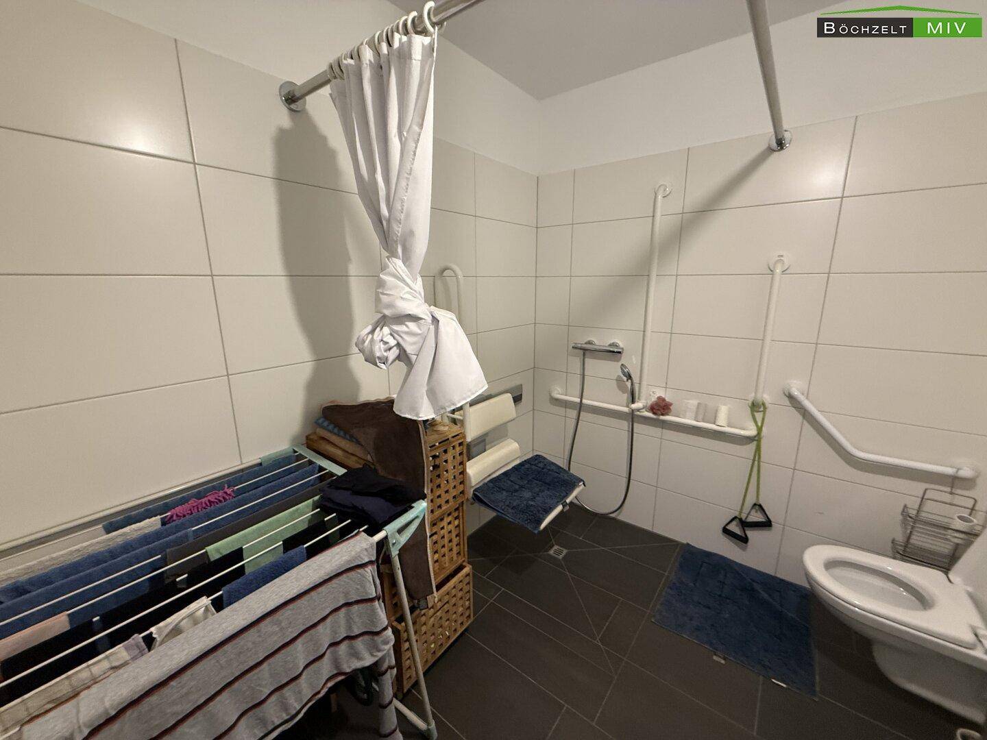 Helles Badezimmer mit barrierefreier Dusche, Haltegriffen und Wäscheständer.