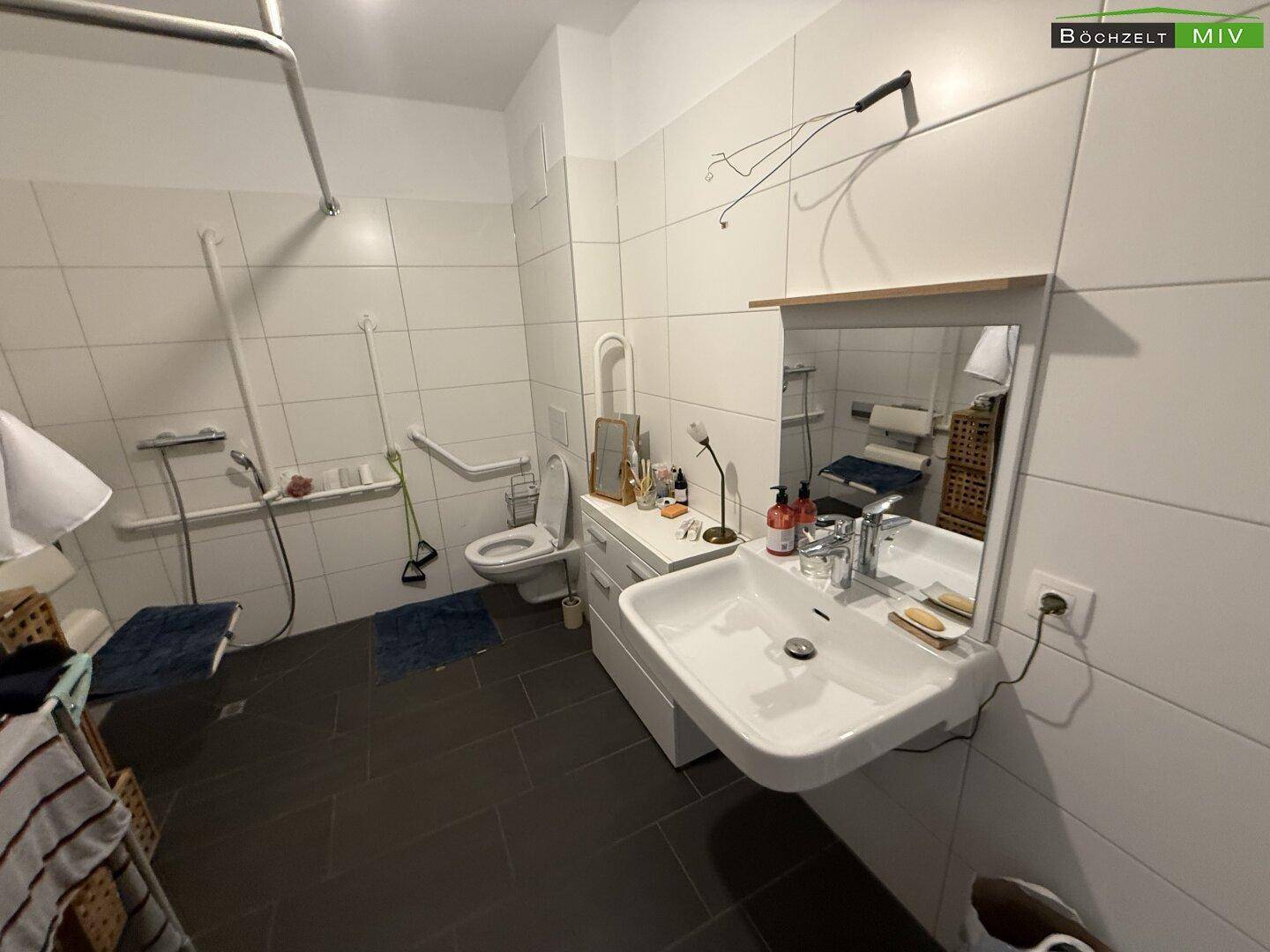 Modernes Badezimmer mit barrierefreier Dusche, WC, großem Spiegel und Haltegriffen.