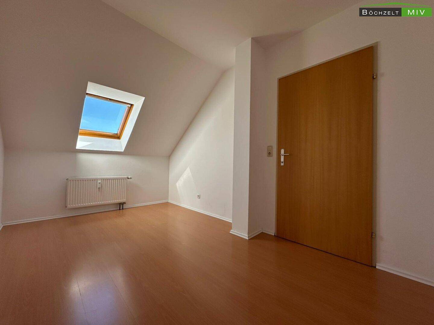 Heller Raum im Dachgeschoss mit Laminatboden, Heizkörper und Dachfenster.
