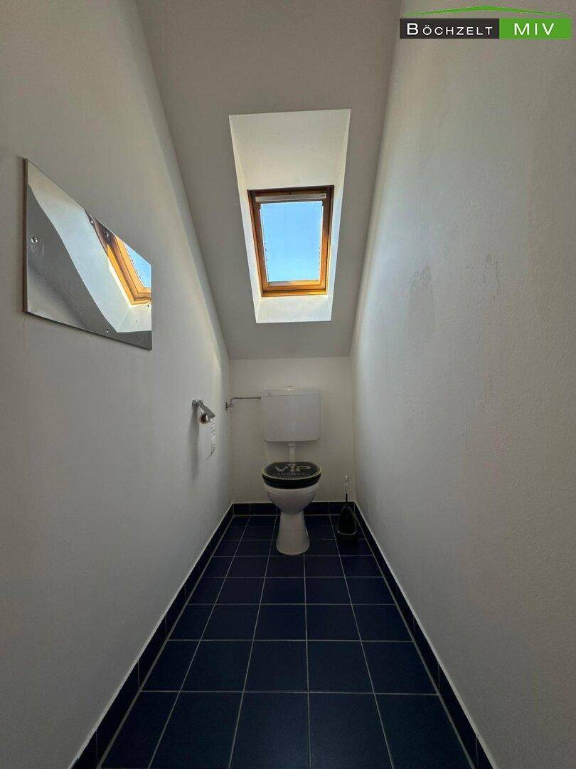 Separates WC im Dachgeschoss mit Toilette, blauen Fliesen und Dachfenster.