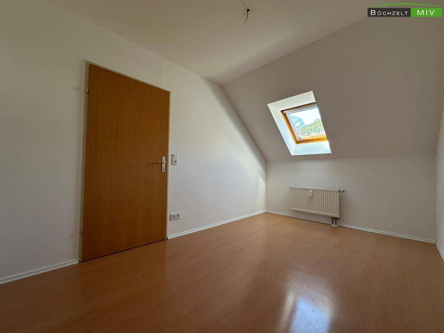Leerer Raum im Dachgeschoss mit Laminatboden, Heizkörper und Dachfenster.
