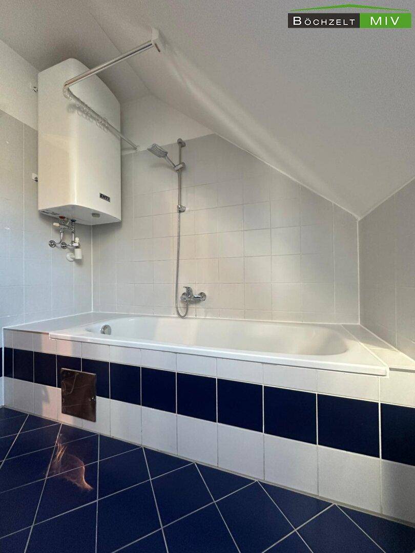 Badezimmer im Dachgeschoss mit Badewanne, blauen Fliesen und Dachschräge.