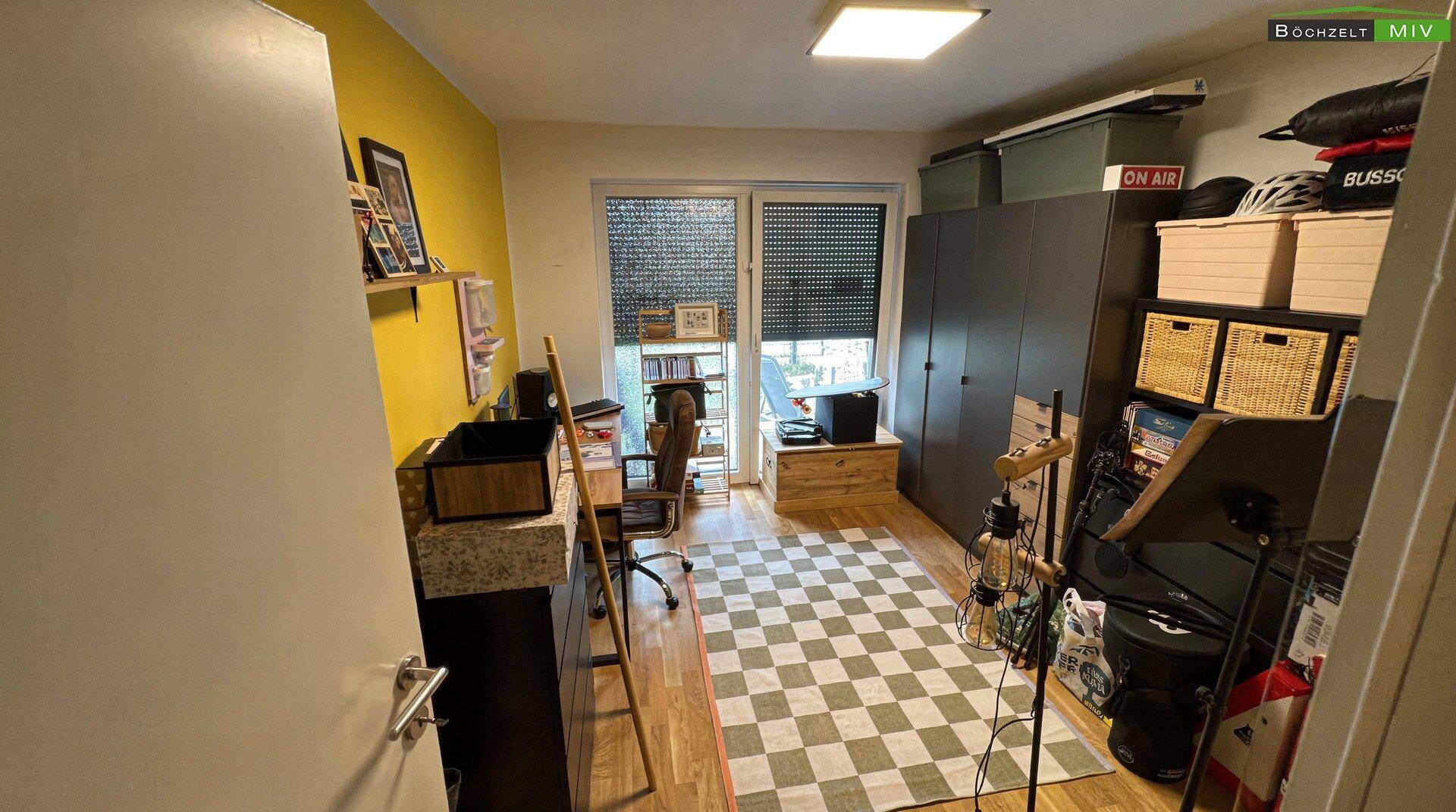Arbeitszimmer mit gelber Akzentwand, Holzboden und Blick ins Grüne.