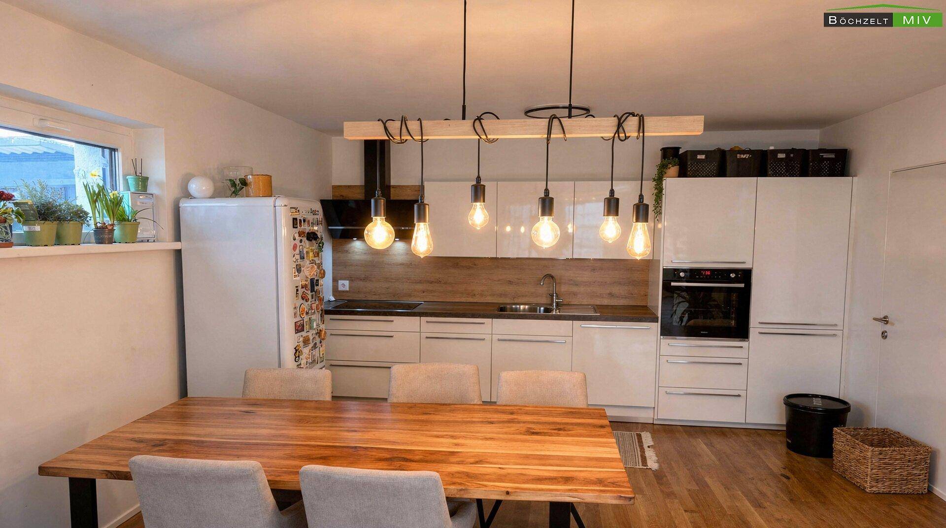 Moderne Einbauküche mit weißen Fronten, Holzarbeitsplatte und Essbereich.