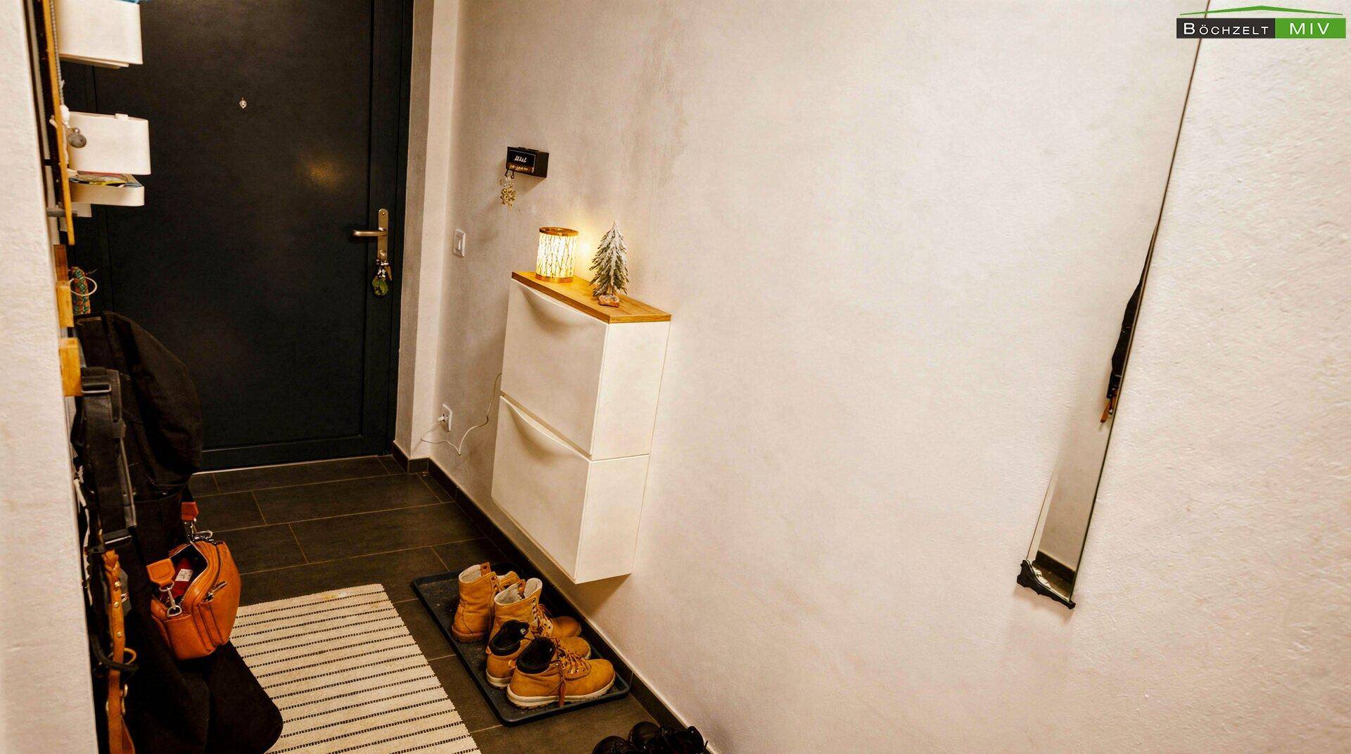 Eingangsbereich mit dunkler Eingangstür, Schuhschrank und Fliesenboden.